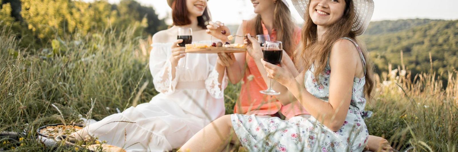 Three women sitting outside eating cheese and drinking wine