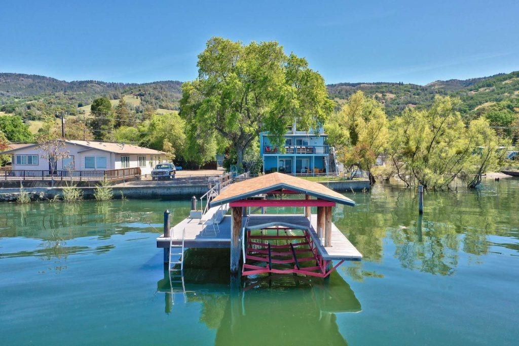 A covered wooden dock with a boat beneath it extends over a calm lakefront.
